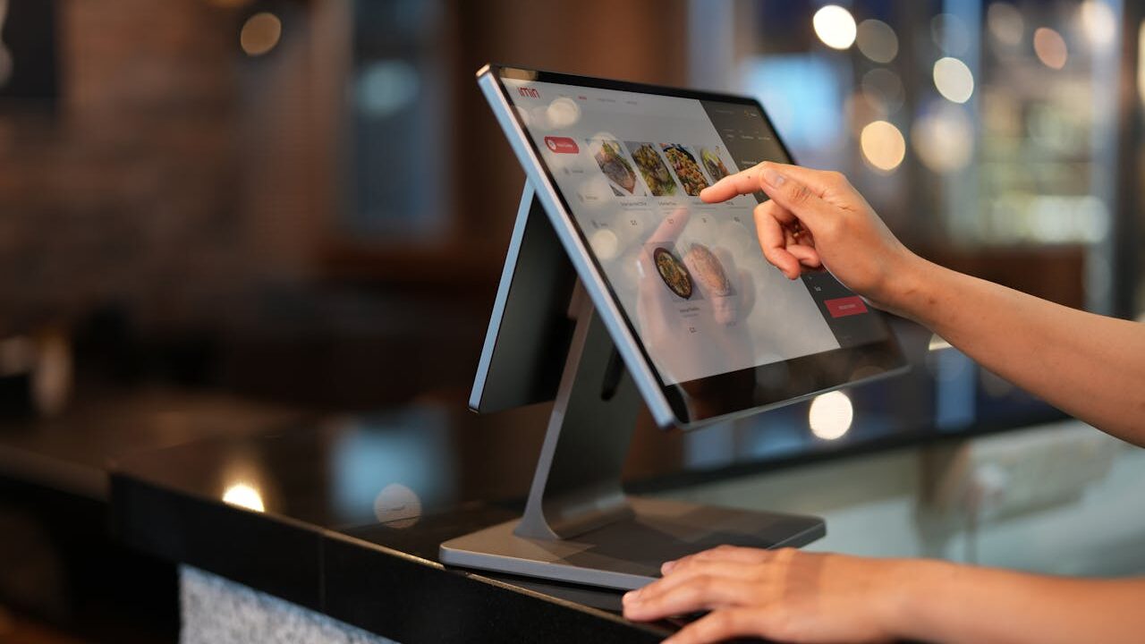 Close-up of a hand interacting with a touchscreen POS system in a restaurant setting.